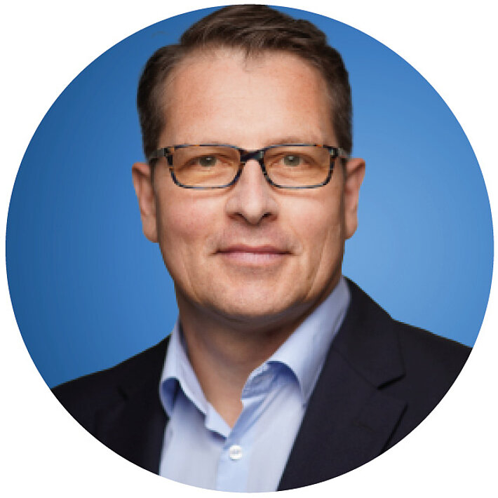 Porträt eines Mannes mit Brille im Anzug vor blauem Hintergrund.