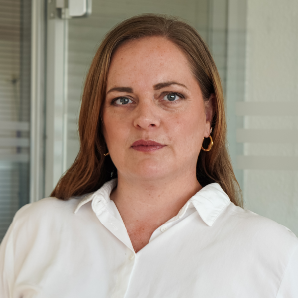Porträt einer Frau mit braunen Haaren und weißem Hemd, die ernst in die Kamera blickt.