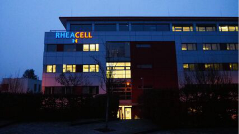 Ein modernes Bürogebäude bei Dämmerung mit beleuchteten Fenstern und dem Schriftzug „RHEACELL“ an der Fassade.