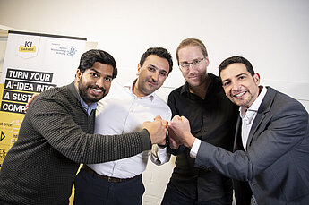 Vier Männer in Businesskleidung stehen eng beieinander und stoßen in der Mitte mit den Fäusten zusammen, als Zeichen von Teamgeist und Zusammenhalt.