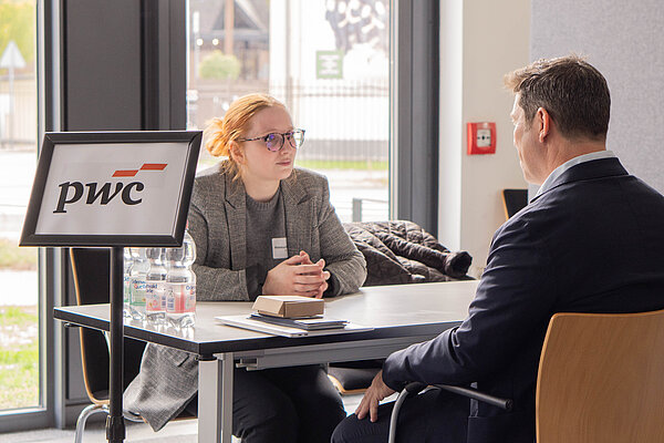 Zwei Personen sitzen sich an einem Tisch gegenüber und führen ein Gespräch bei einer PwC-Veranstaltung.